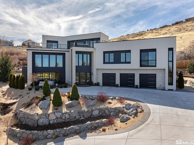 contemporary home featuring a garage, driveway, a balcony, and stucco siding