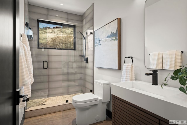 bathroom with a stall shower, vanity, toilet, and wood finished floors