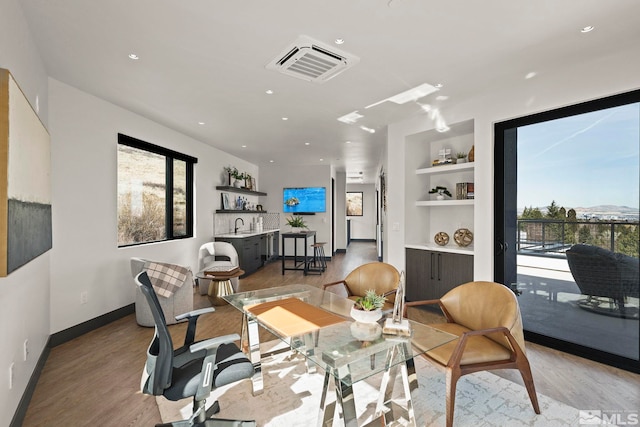 home office with built in shelves, a sink, visible vents, baseboards, and light wood-style floors