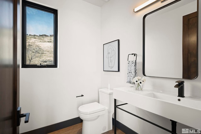 bathroom featuring toilet, a sink, baseboards, and wood finished floors