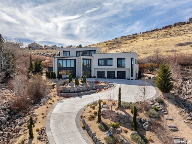 contemporary house with a garage, driveway, a balcony, fence, and stucco siding