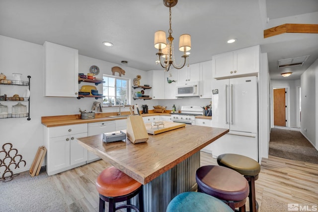 kitchen with a breakfast bar area, white appliances, white cabinetry, wooden counters, and open shelves