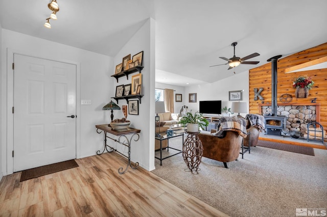 living room featuring a wood stove, ceiling fan, vaulted ceiling, and wood finished floors