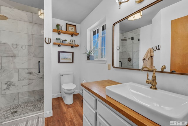 bathroom with toilet, a shower stall, vanity, wood finished floors, and baseboards