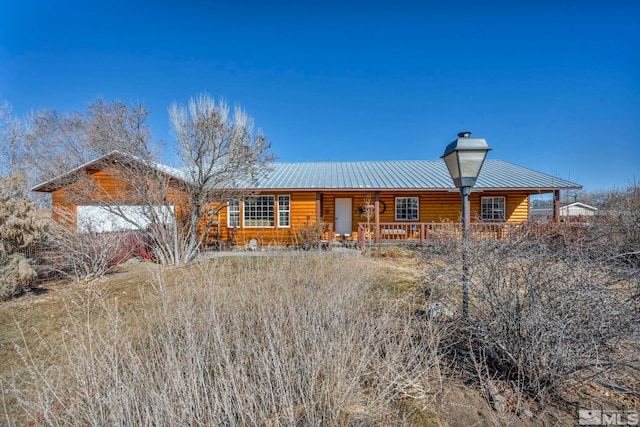 view of front of house featuring a porch, log veneer siding, metal roof, and a chimney