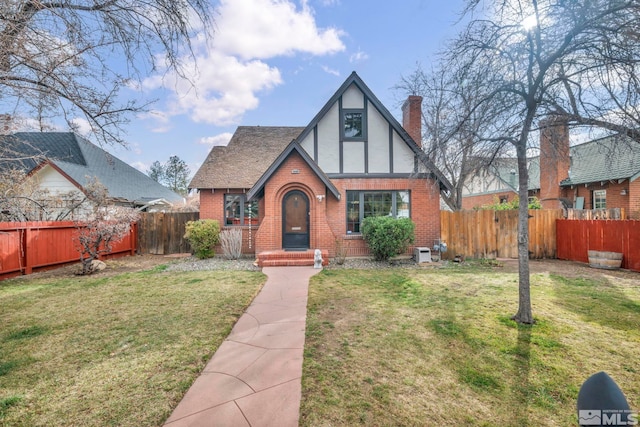 english style home with a chimney, fence, a front lawn, and brick siding