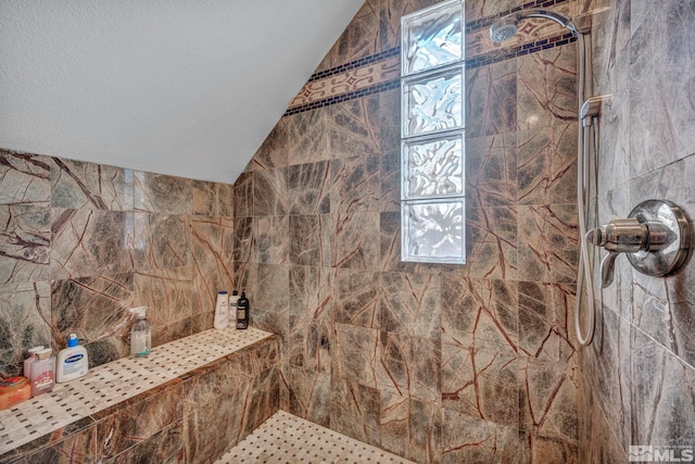 bathroom featuring vaulted ceiling, a tile shower, and a textured ceiling