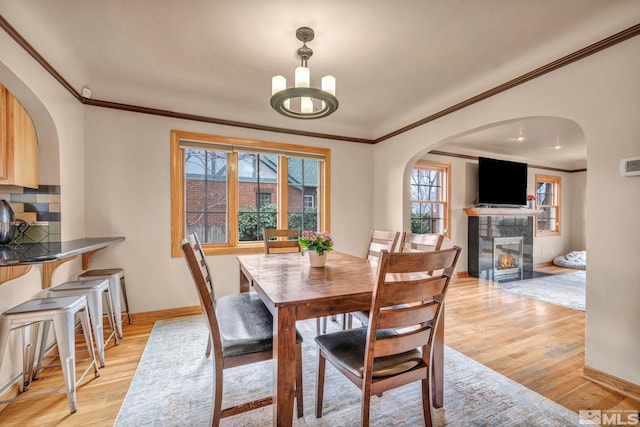 dining area with ornamental molding, a tiled fireplace, light wood-style flooring, and baseboards