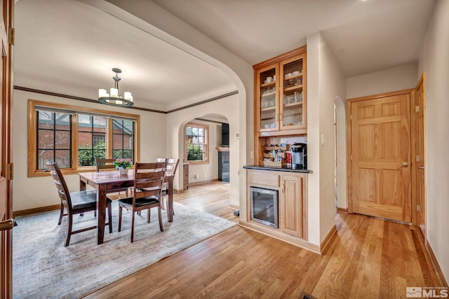 dining space with arched walkways, light wood-style flooring, an inviting chandelier, ornamental molding, and baseboards