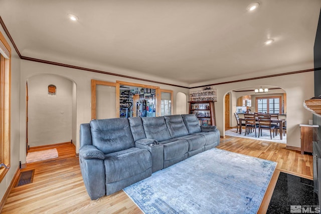 living area with arched walkways, crown molding, visible vents, and light wood-style floors