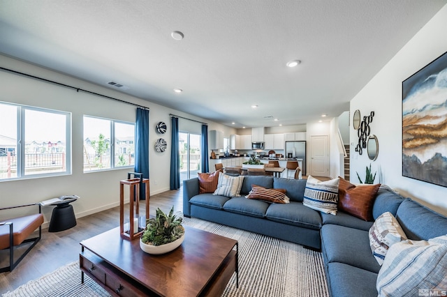 living room featuring recessed lighting, visible vents, baseboards, stairway, and light wood-type flooring