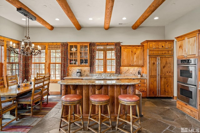 kitchen with a wealth of natural light, stainless steel double oven, stone tile flooring, and tasteful backsplash