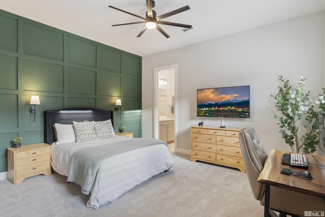 bedroom featuring visible vents, a ceiling fan, light colored carpet, ensuite bathroom, and a decorative wall