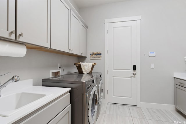 washroom featuring baseboards, cabinet space, a sink, and washing machine and clothes dryer