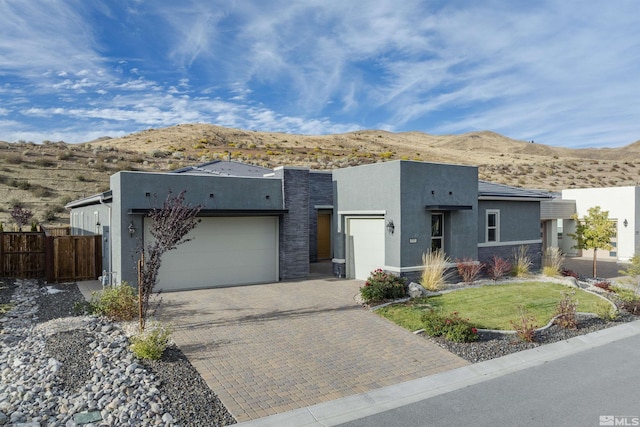 view of front of property featuring an attached garage, fence, decorative driveway, a mountain view, and stucco siding