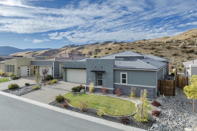 view of front of house featuring decorative driveway, stucco siding, a mountain view, fence, and a garage