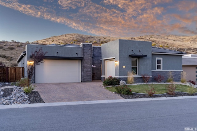 view of front facade featuring stone siding, an attached garage, decorative driveway, a mountain view, and stucco siding