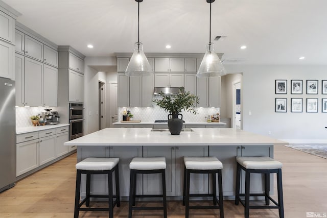 kitchen with light wood-style flooring, gray cabinetry, stainless steel appliances, visible vents, and a center island with sink