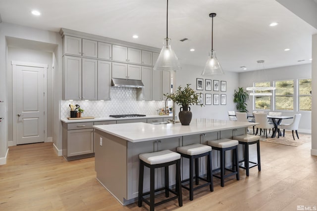 kitchen featuring under cabinet range hood, light wood-type flooring, gas stovetop, and gray cabinetry