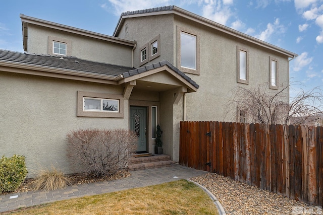 doorway to property featuring a tile roof, fence, and stucco siding