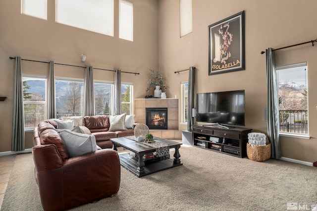 living area featuring a high ceiling, baseboards, and a tiled fireplace