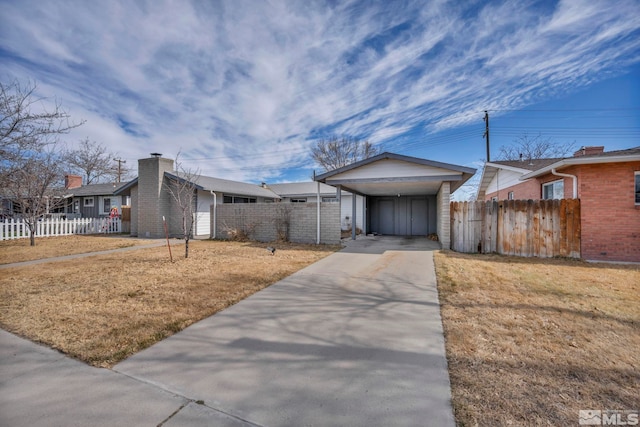 view of front facade featuring concrete driveway, a chimney, fence, a front yard, and brick siding