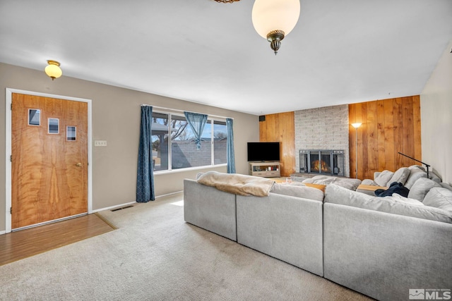 living area featuring wooden walls, carpet flooring, visible vents, baseboards, and a brick fireplace