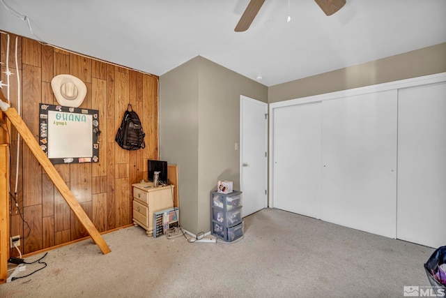 interior space with a ceiling fan, carpet, and wood walls