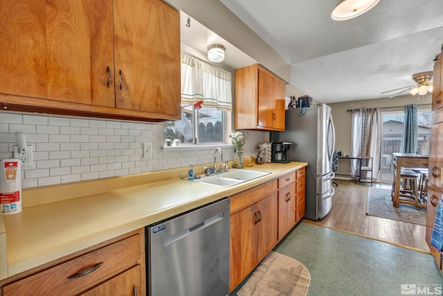 kitchen featuring stainless steel appliances, light countertops, brown cabinetry, a ceiling fan, and a sink