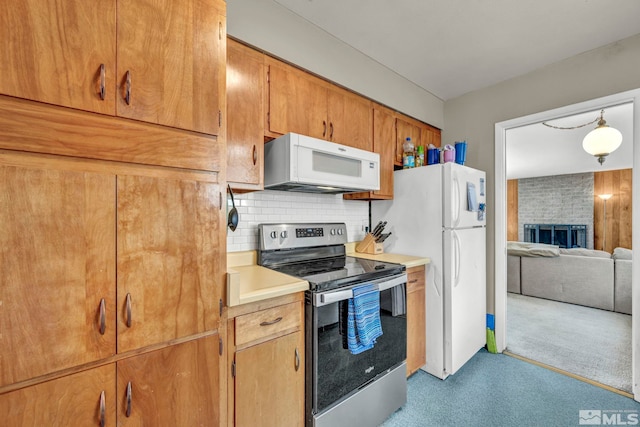 kitchen with brown cabinets, tasteful backsplash, light countertops, a brick fireplace, and white appliances