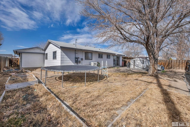 rear view of house with an outbuilding, a fenced backyard, a storage shed, a garden, and a trampoline