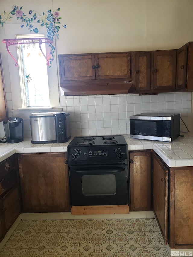 kitchen featuring stainless steel microwave, tile counters, black electric range oven, and under cabinet range hood