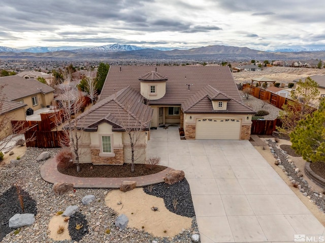 view of front of house featuring stucco siding, concrete driveway, a mountain view, fence, and stone siding