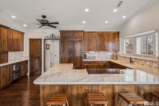 kitchen featuring black electric stovetop, visible vents, a sink, light stone countertops, and paneled fridge