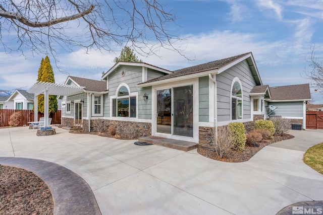 exterior space featuring stone siding, a patio area, fence, and a pergola