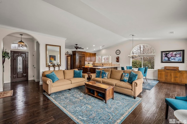 living room with arched walkways, a notable chandelier, dark wood-type flooring, vaulted ceiling, and ornamental molding