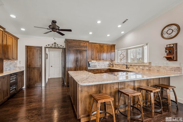 kitchen featuring ornamental molding, a breakfast bar, a peninsula, and light stone countertops