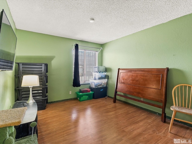 bedroom featuring a textured ceiling, baseboards, and wood finished floors