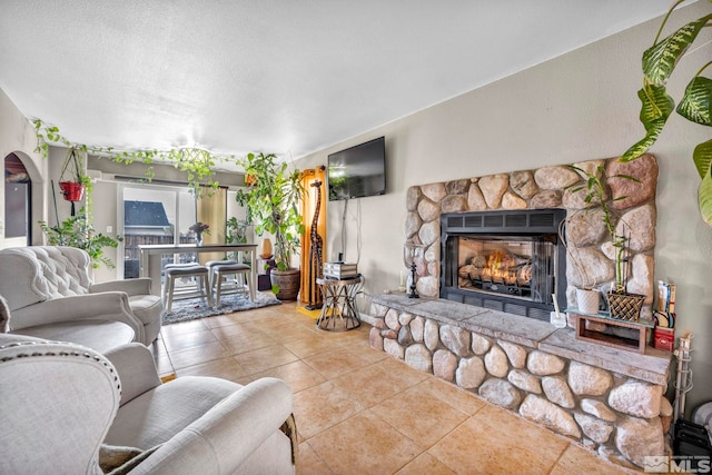 living room featuring a textured ceiling, arched walkways, a fireplace, and tile patterned flooring