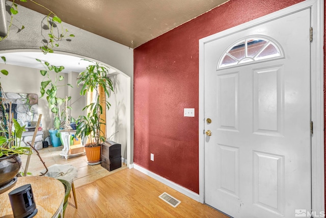 entrance foyer with arched walkways, a textured wall, wood finished floors, visible vents, and baseboards