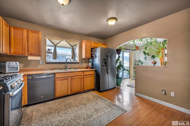 kitchen with light wood finished floors, light countertops, appliances with stainless steel finishes, a sink, and a textured ceiling