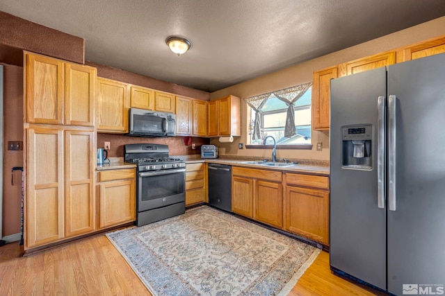 kitchen featuring light countertops, a sink, a textured ceiling, light wood-type flooring, and black appliances