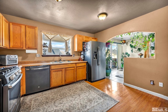 kitchen with a toaster, light wood-style flooring, stainless steel appliances, light countertops, and a sink