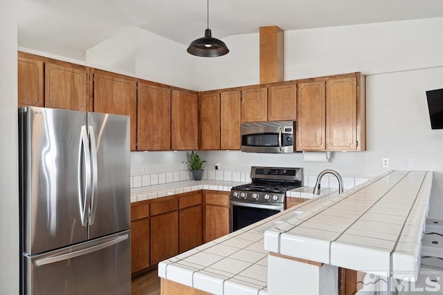 kitchen with tile countertops, a peninsula, appliances with stainless steel finishes, and brown cabinets