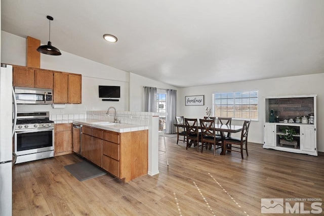 kitchen featuring stainless steel appliances, a peninsula, wood finished floors, a sink, and tile counters