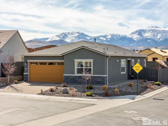 view of front of house featuring a garage, stone siding, fence, a mountain view, and stucco siding