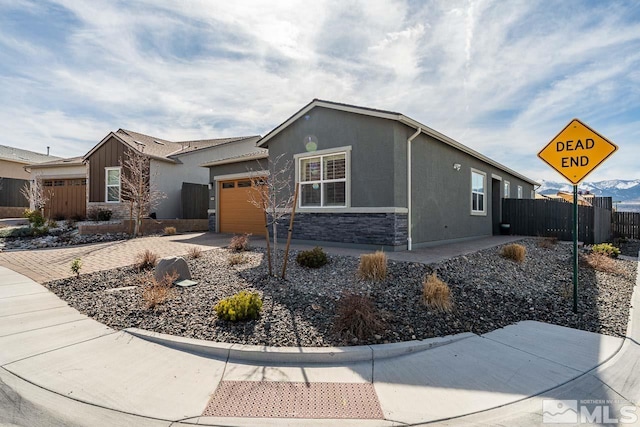 view of front facade featuring an attached garage, fence, stone siding, driveway, and stucco siding