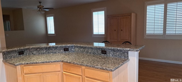 kitchen featuring a ceiling fan, stone counters, baseboards, and wood finished floors