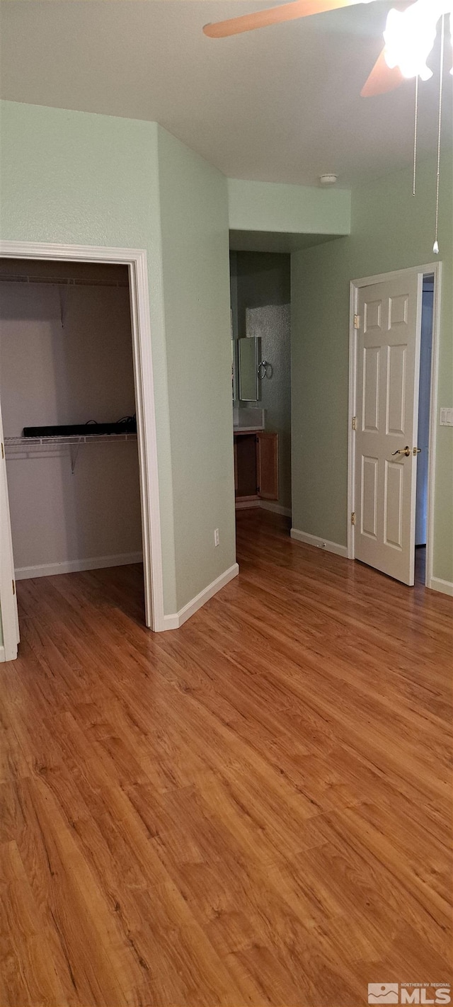 unfurnished bedroom with a closet, wood finished floors, a walk in closet, and baseboards