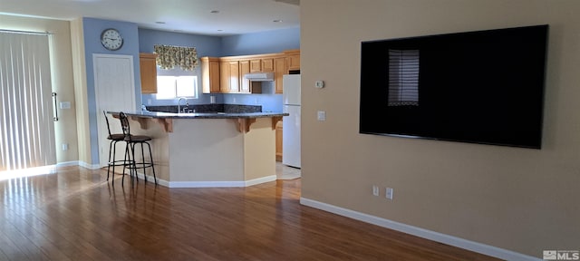 kitchen with light wood-style flooring, a breakfast bar area, freestanding refrigerator, and baseboards